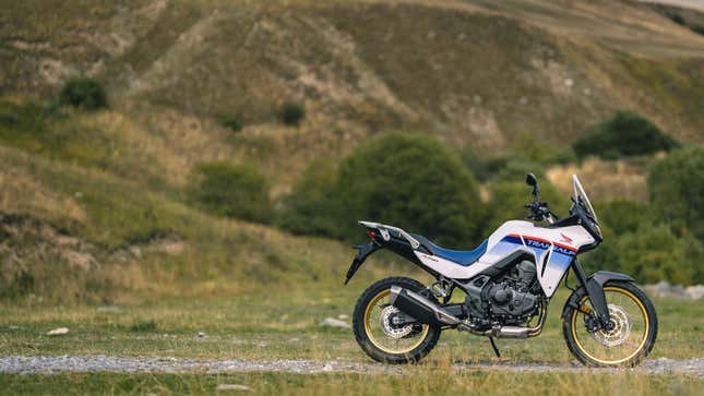 緑の山の前の砂利道に座るホンダ トランザルプ